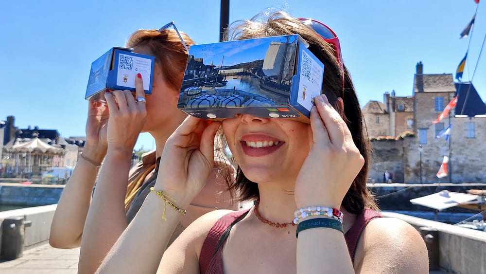Deux visiteuses regardent une reconstitution à travers des lunettes de réalité virtuelle Legendr, sur le port de Honfleur.